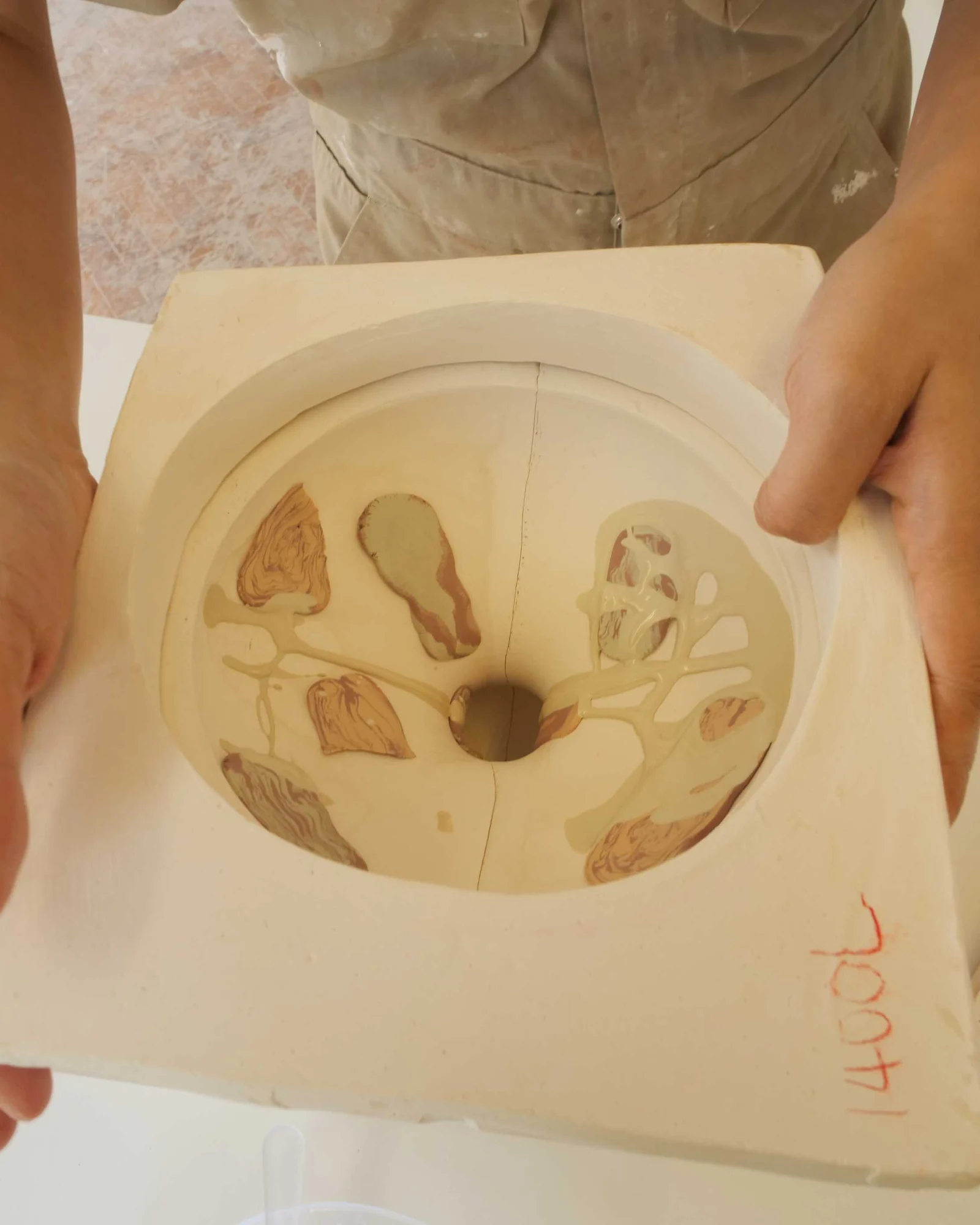 Hands lifting a decorated slipcast Moonjar from its plaster mould