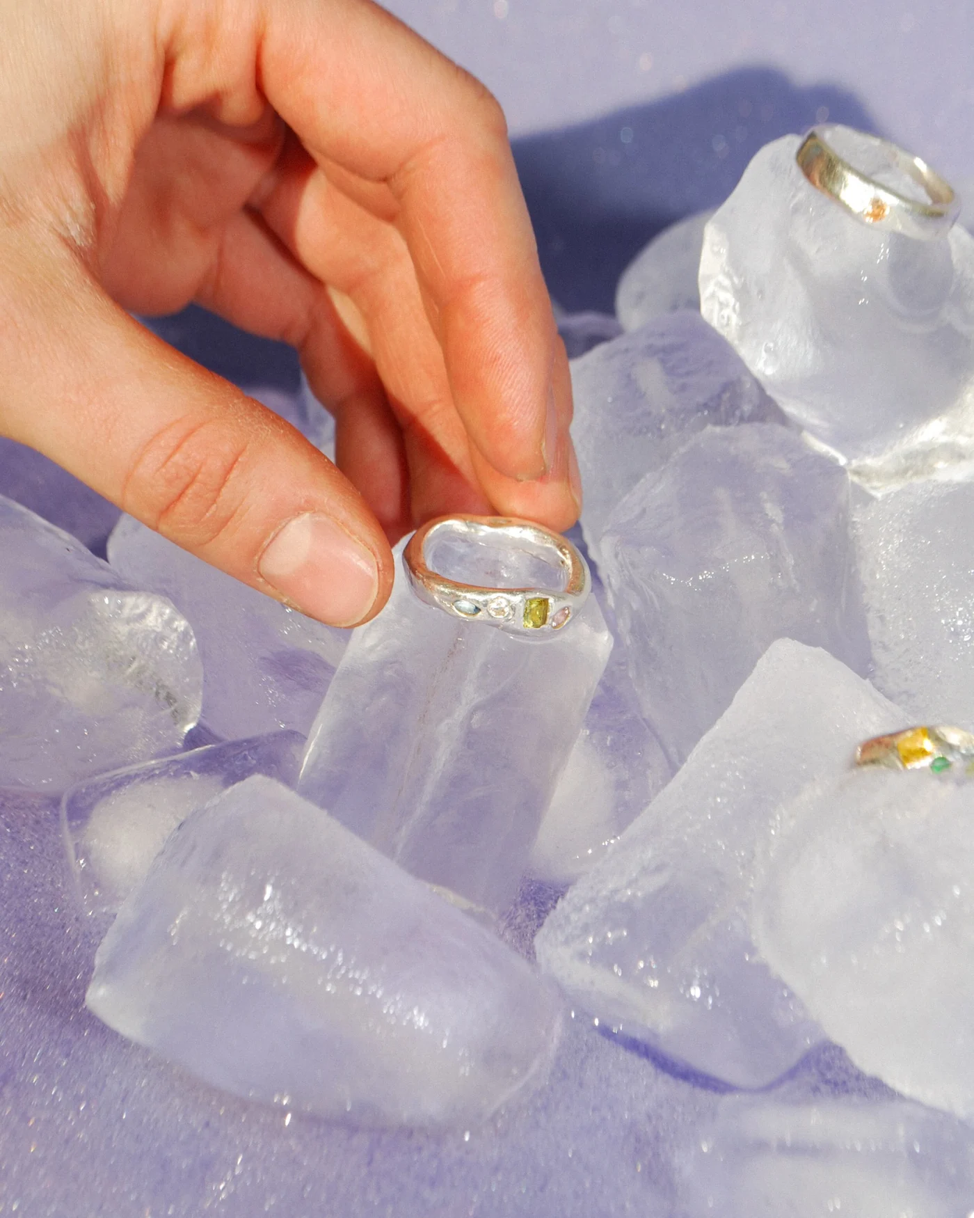 Handmade silver ring with embedded colourful gemstones displayed on ice cubes